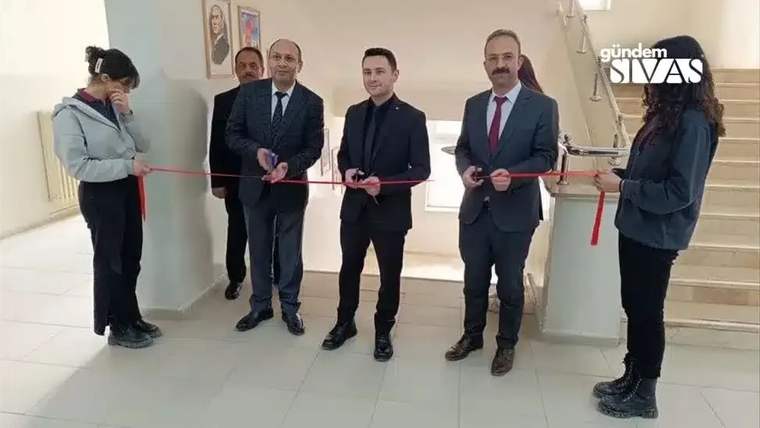 Kurdele kesen beş kişi, arka planda genç ressamların eserleri sergileniyor.
