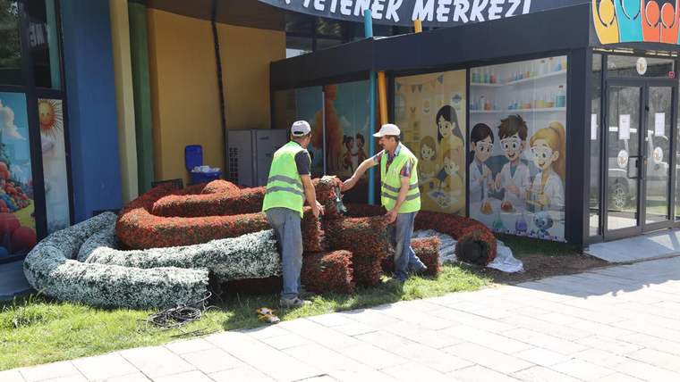 İki kişi, çocuk yetenek merkezinin önünde çiçek düzenlemesi yapıyor.