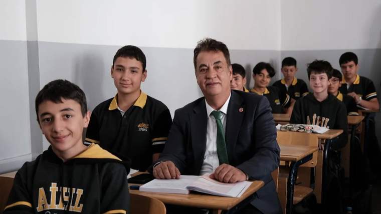 Sınıfta oturan bir grup öğrenci ve yanında bir kişi, hepsi gülümsüyor.