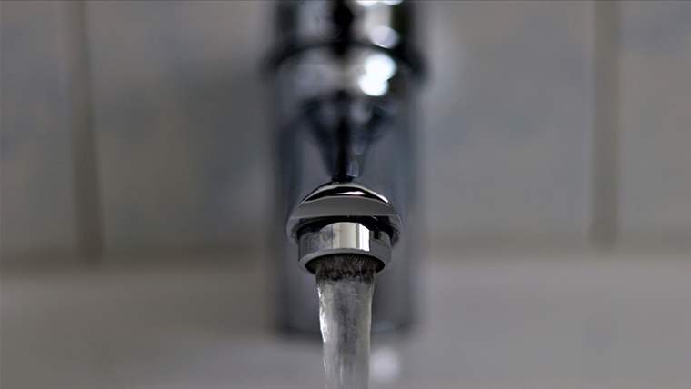 Bir musluktan akan su, metal bir lavabo üzerinde görünmekte.
