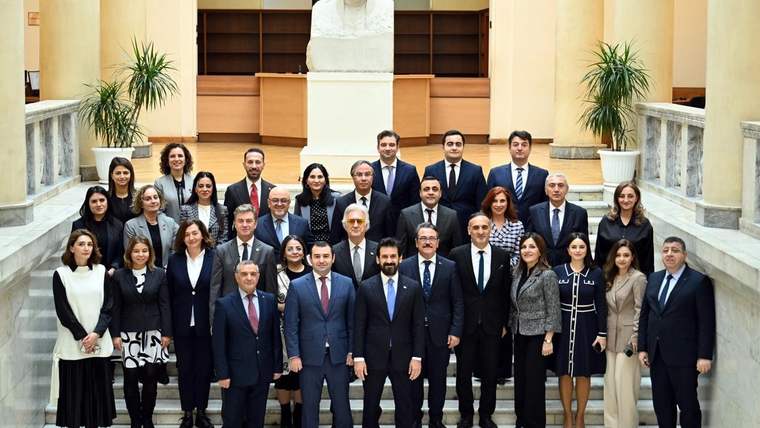Bir grup insan, bir binanın içinde poz veriyor; arka planda bir heykel ve bitkiler var.