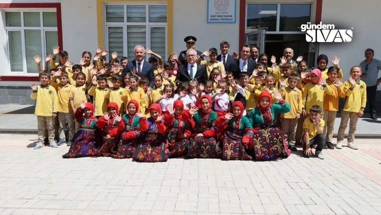 Okul bahçesinde, geleneksel kıyafetler giymiş öğrenciler ve yetişkinler gülümseyerek poz veriyor.