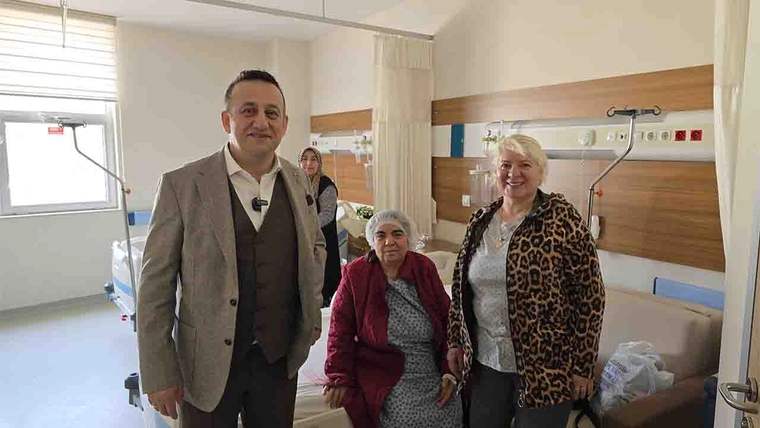 Hastane odasında bir kadın yatakta otururken yanında iki kadın ve bir erkek ayakta duruyor; tıbbi ekipman görülüyor.