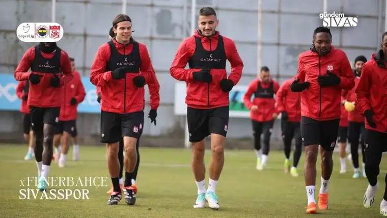 Kırmızı antrenman kıyafetleri giymiş dört futbolcu, antrenman sahasında koşuyor.