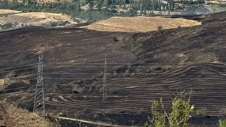 Kuru arazide yanmış alanlar ve elektrik direkleri görünmekte.