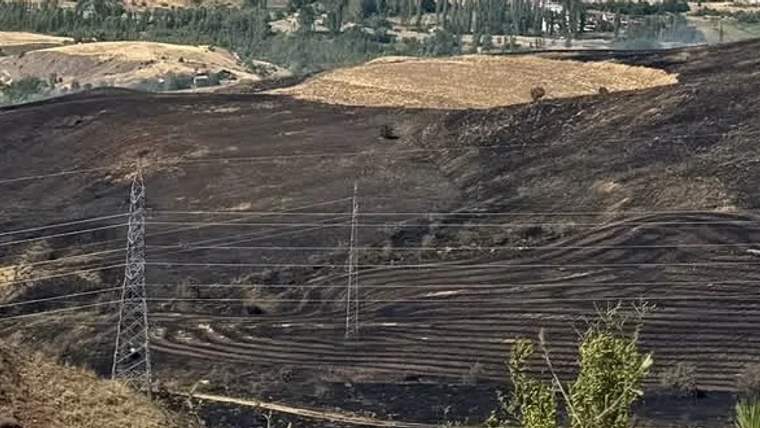 Kuru arazide yanmış alanlar ve elektrik direkleri görünmekte.