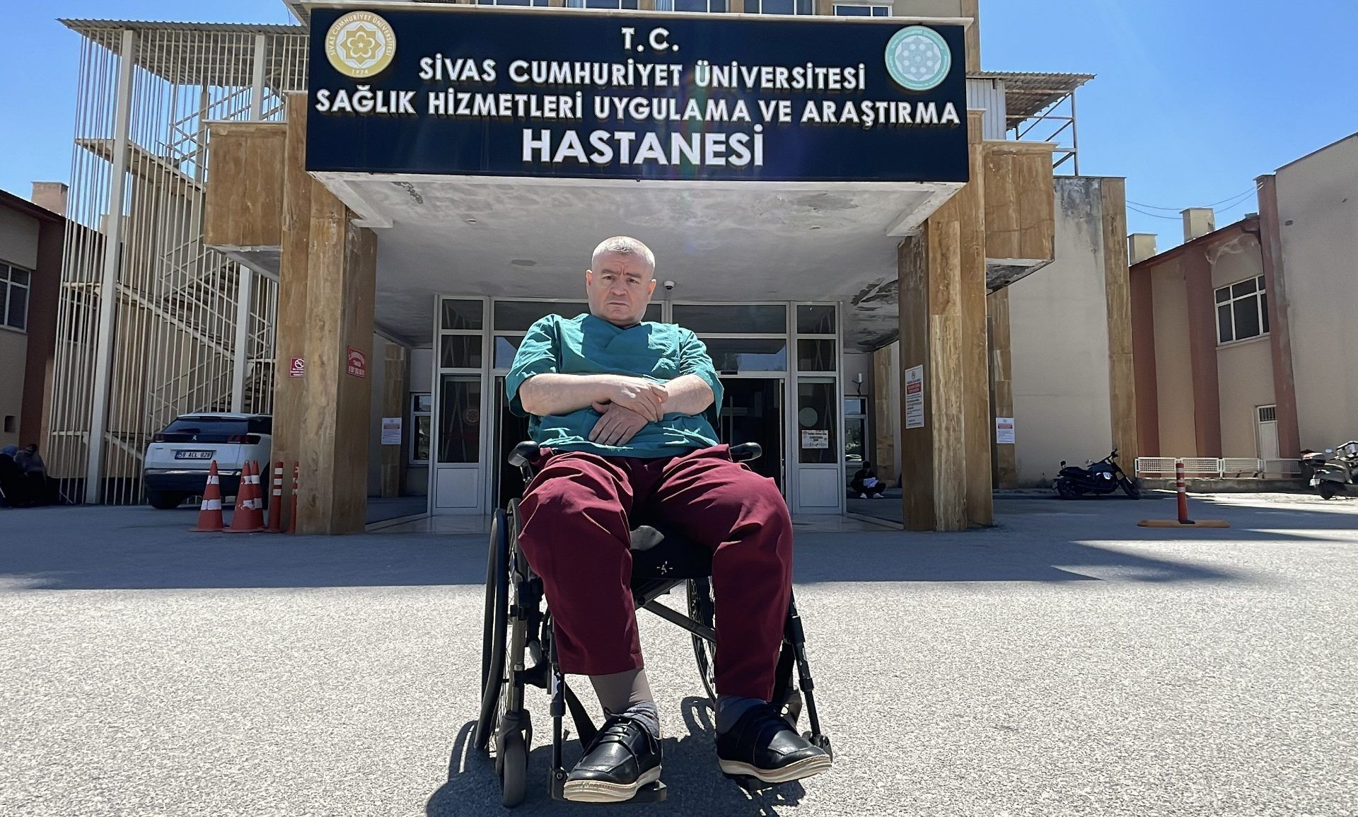 Bir tekerlekli sandalyede oturan bir kişi, hastane binasının önünde duruyor.