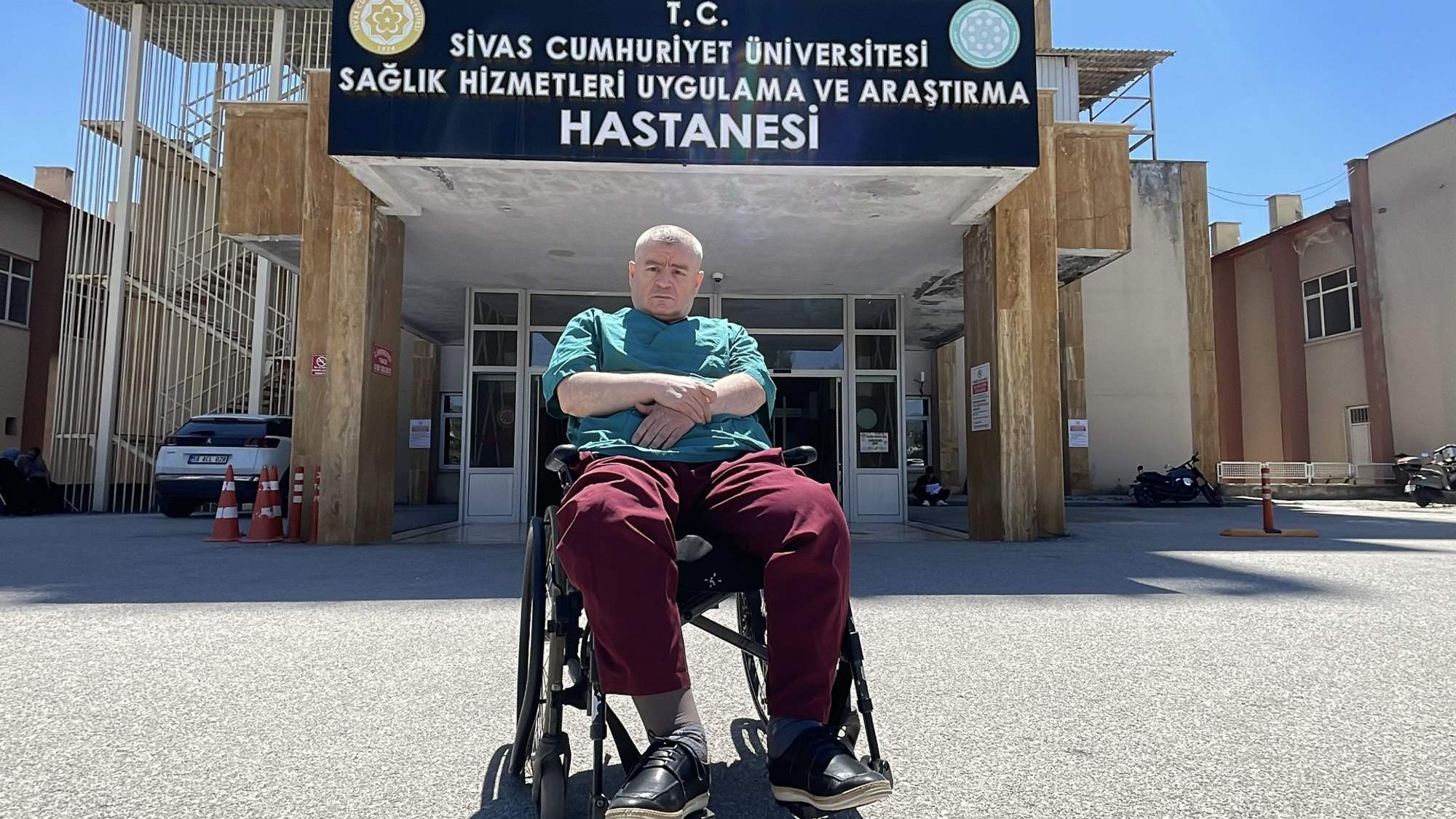 Bir tekerlekli sandalyede oturan bir kişi, hastane binasının önünde duruyor.