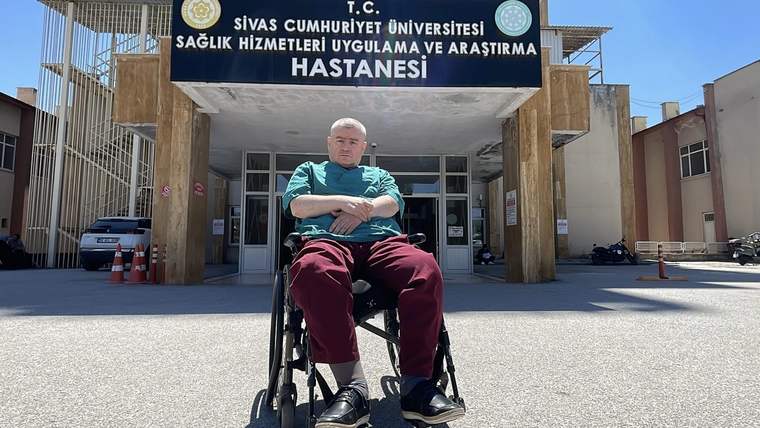 Bir tekerlekli sandalyede oturan bir kişi, hastane binasının önünde duruyor.