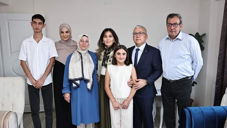 Bir evin salonunda, aralarında başörtülü kadın ve çocuk bulunan yedi kişi yan yana duruyor.