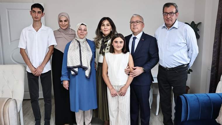 Bir evin salonunda, aralarında başörtülü kadın ve çocuk bulunan yedi kişi yan yana duruyor.