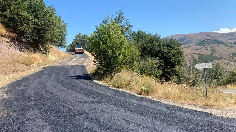 Asfalt yama çalışmaları tamamlanan yol, ağaçlarla çevrili bir alanda görünmekte.