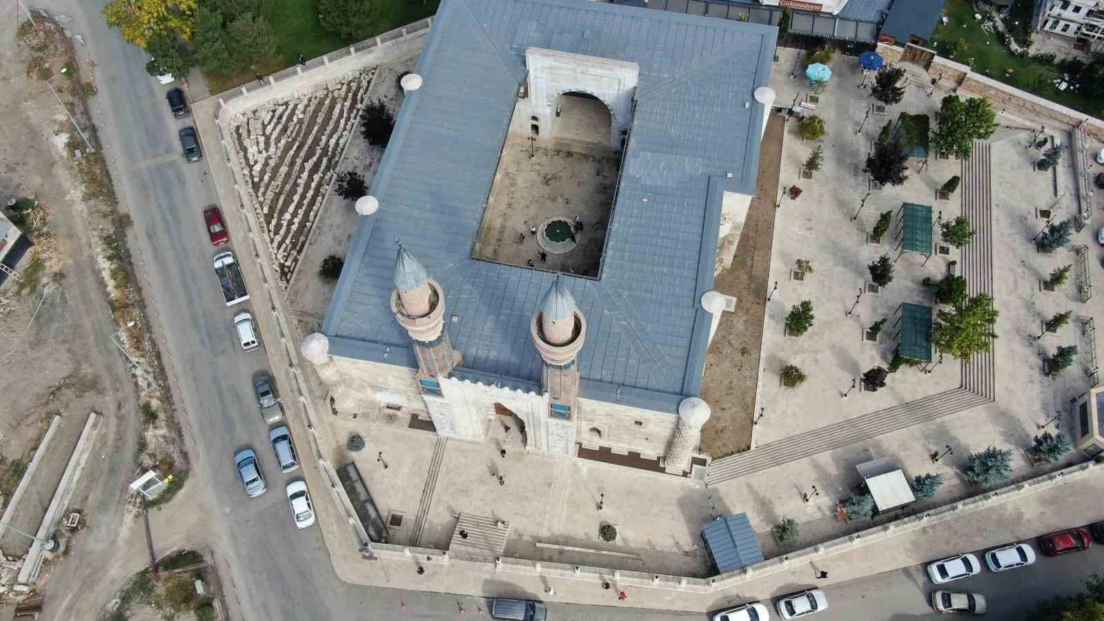 Havadan görülen iki minareli cami, çevresindeki avlu, ağaçlı alan ve yollarla birlikte kadrajda yer alıyor.