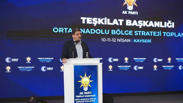 Mikrofonun önünde bir kişi, arkasında AK Parti'nin strateji toplantısı için hazırlanmış sahne dekoru var.