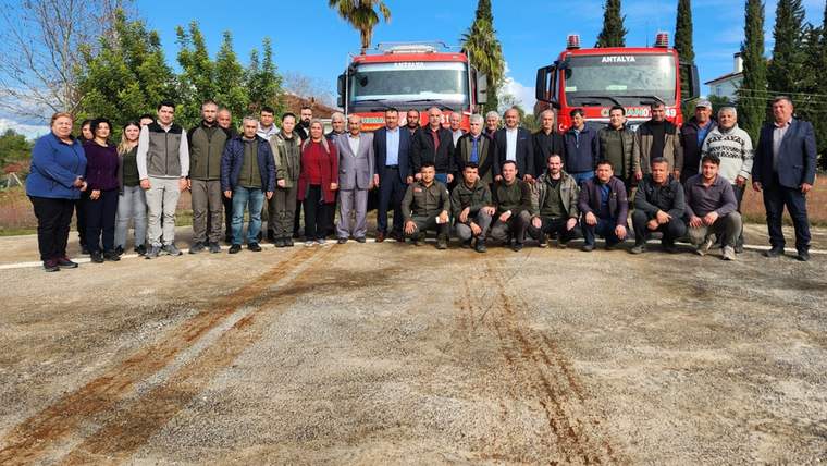Yangın söndürme araçlarının önünde bir grup insan, bilgilendirme toplantısında bir araya gelmiş.