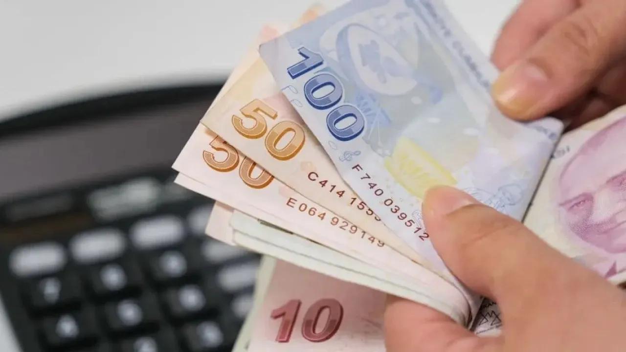 Elde, farklı kupürlerde Türk lirası banknotları tutuluyor; arka planda bilgisayar klavyesi görülüyor.