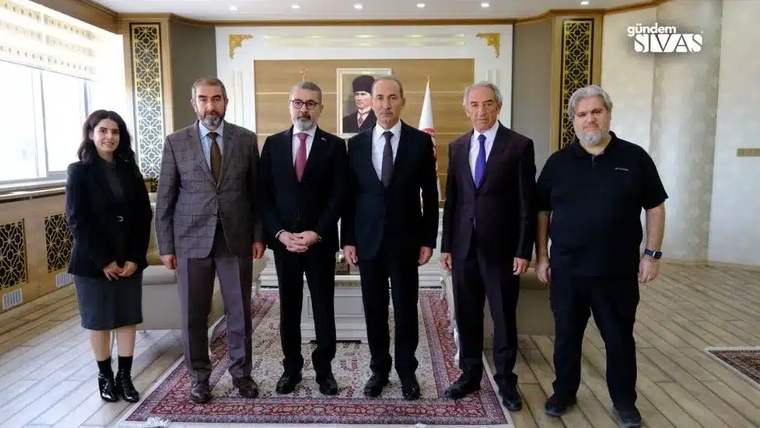 Altı kişi, bir odada yan yana duruyor; arka planda Türk bayrağı ve Atatürk portresi var.