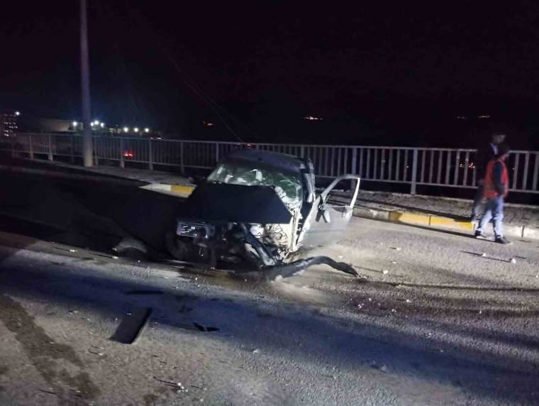Gece köprü yolunda ön kısmı hasar görmüş bir otomobil, açık kapısıyla yol üzerinde duruyor.
