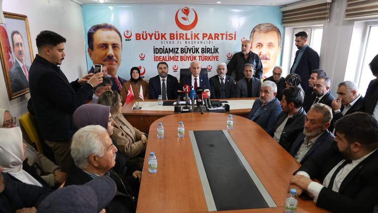 Büyük Birlik Partisi toplantı salonunda, masanın etrafında oturan kalabalık bir grup insan, konuşan bir kişiyi dinliyor.