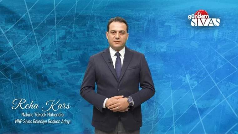 Mavi arka planda, elinde mikrofon tutan bir kişi, resmi kıyafetle konuşma yapıyor.