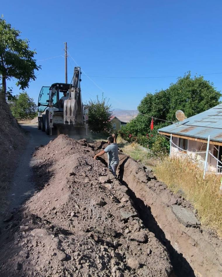 Bir işçi, kazı yapılan yolda çalışırken, arka planda bir iş makinesi yer alıyor.