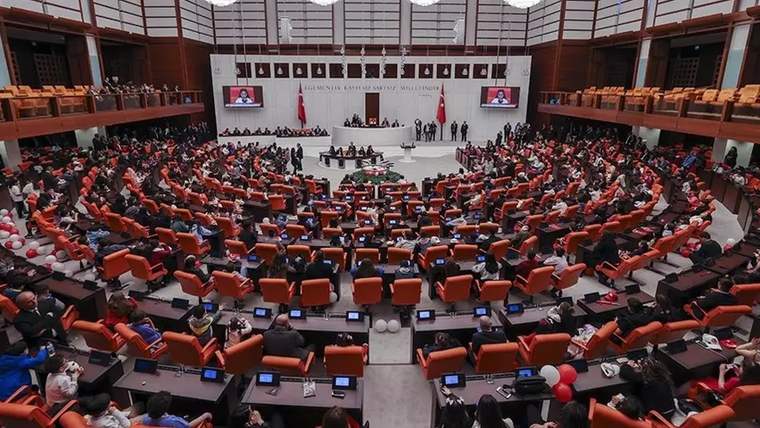 Türk bayrakları ve kürsünün bulunduğu parlamento salonunda çok sayıda kişi sıralarda oturuyor.