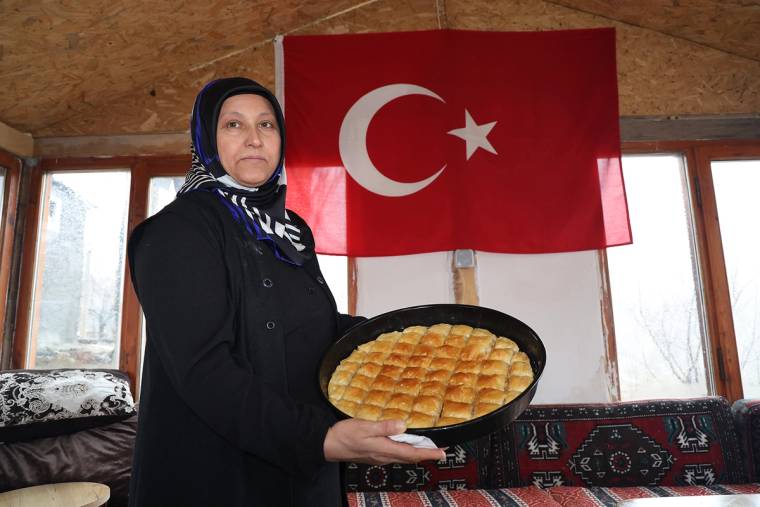 Başörtülü bir kadın, arkasındaki Türk bayrağı önünde dilimlenmiş baklava tepsisi tutuyor.