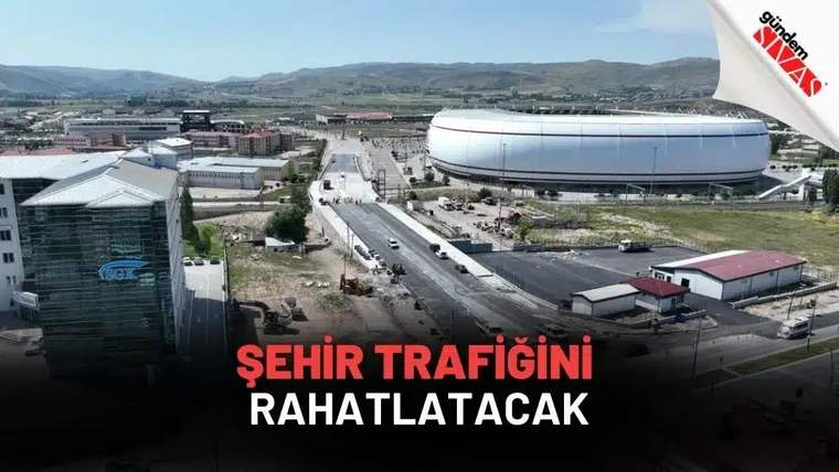 Havadan görünümde, çok şeritli bir yolun yanında büyük oval bir yapı ve çevresindeki binalar görülüyor.