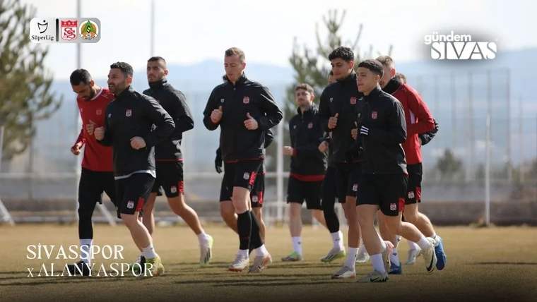 Spor kıyafetleri giyen bir grup futbolcu, açık hava sahasında birlikte koşuyor.