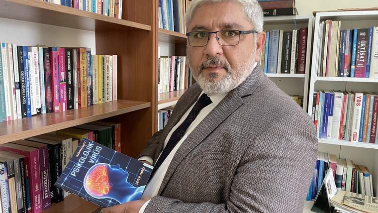 Bir adam, kitap rafının önünde elinde bir kitap tutuyor.
