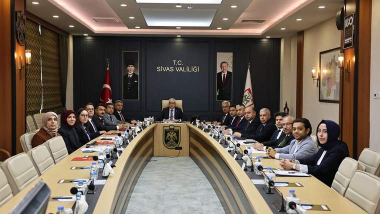 T.C. Sivas Valiliği yazılı salonda, Türk bayrağı ve amblemin önünde uzun masa çevresinde kişiler oturuyor.