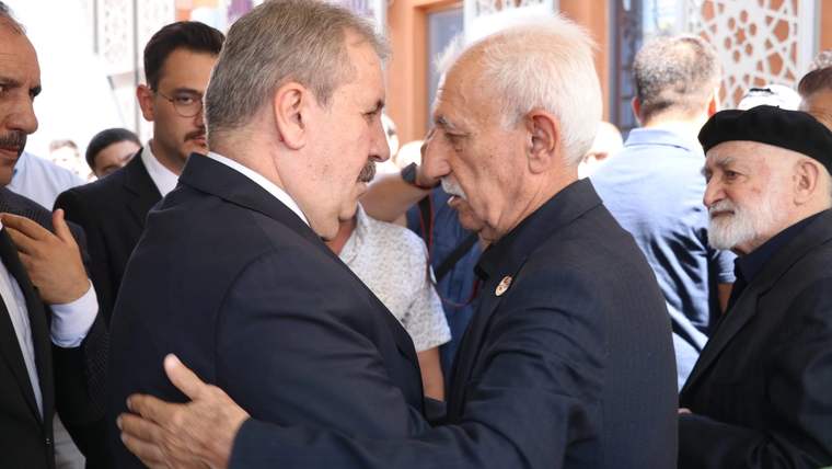 Bir binanın girişinde takım elbiseli iki erkek tokalaşırken çevrelerinde kalabalık insanlar duruyor.