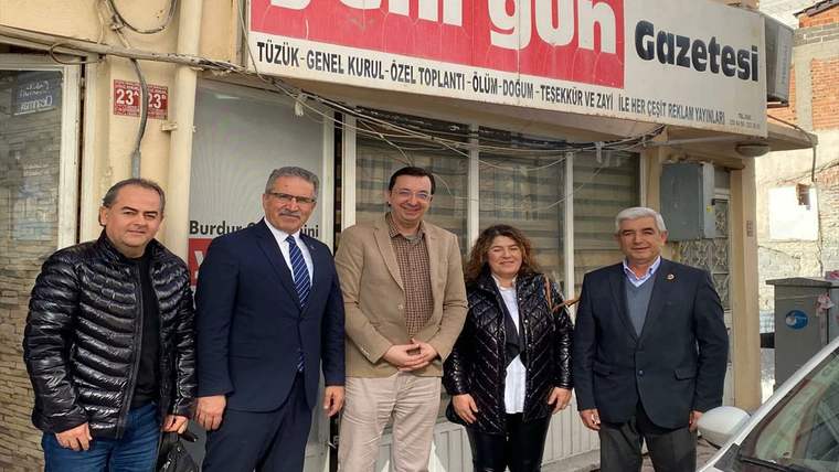 Beş yetişkin, üzerinde “Gazetesi” yazan bir iş yerinin önünde yan yana duruyor.