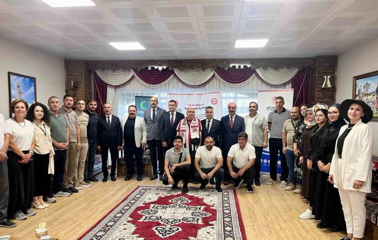 Salonun ortasında, halı üzerinde sıralanan kalabalık bir grup birlikte poz veriyor.