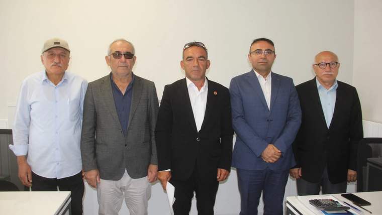 Beş kişi, bir toplantı odasında yan yana duruyor. Bazıları gözlük takıyor ve farklı kıyafetler giymiş.