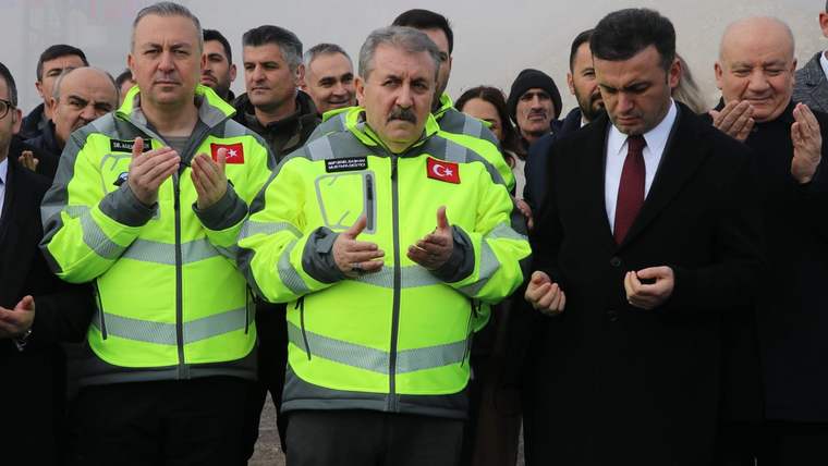 Açılış töreninde, yeşil yelek giymiş üç kişi dua ediyor, arka planda kalabalık bir grup yer alıyor.