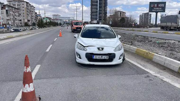 Bir otomobil, yol kenarında duruyor; ön kısmında hasar var, çevresinde trafik koni ve iş makineleri görünmekte.