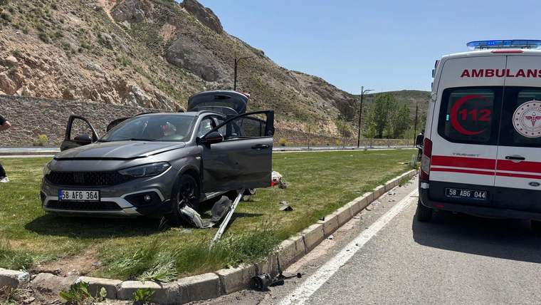 Kavşak kenarındaki çim alanda hasar görmüş otomobil ve yanında duran ambulans görülüyor.