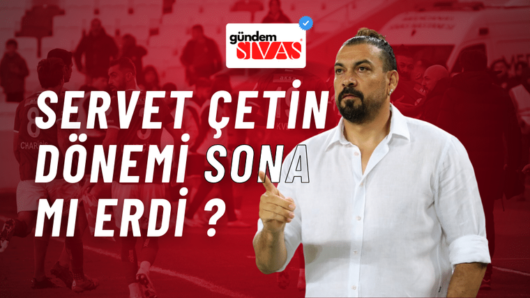 Beyaz gömlek giymiş bir adam, elini yukarı kaldırarak konuşuyor.