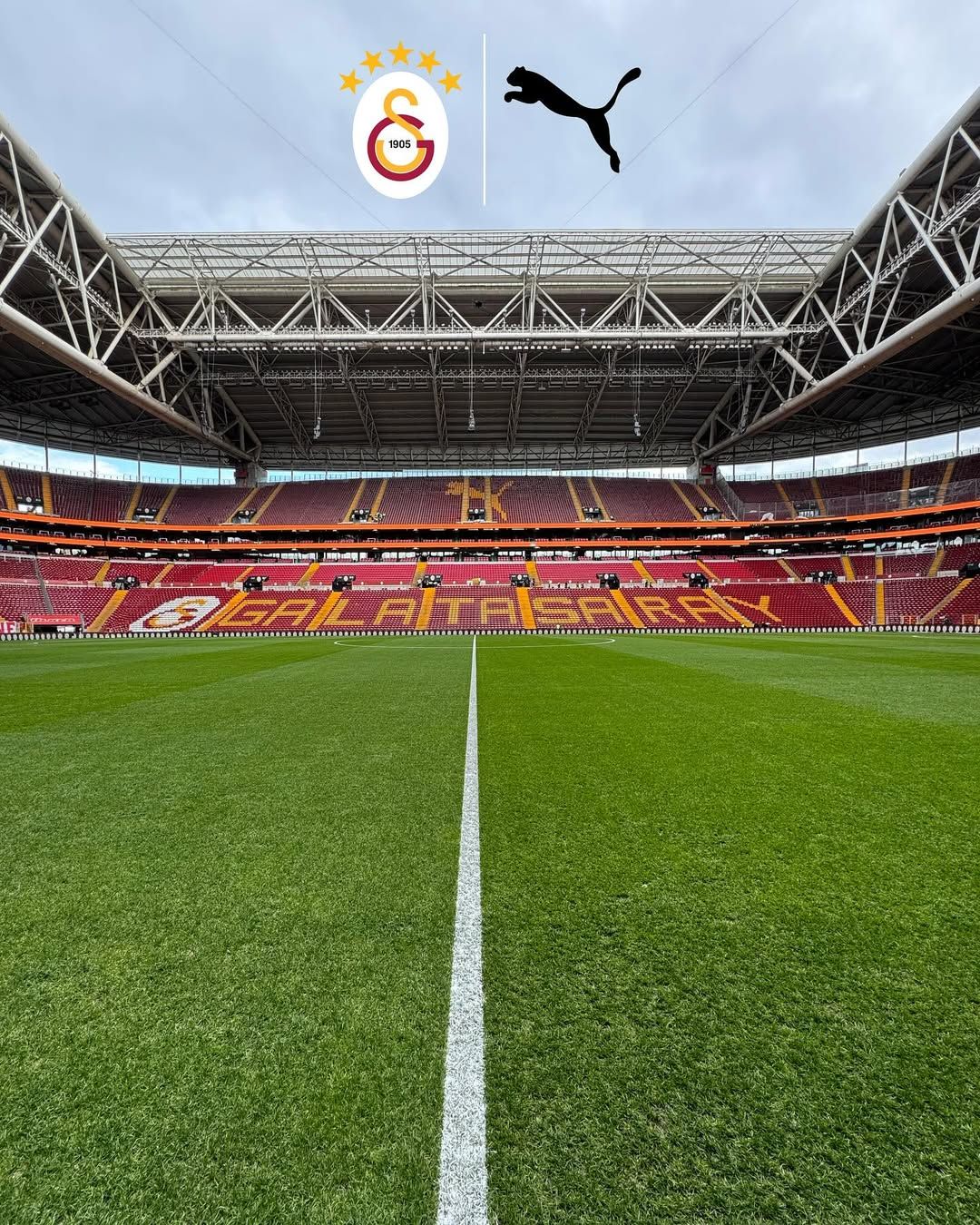 Galatasaray yazılı tribünleri ve yeşil futbol sahası görünen, çatılı bir stadyum içi