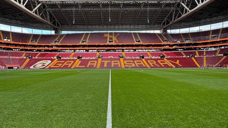 Galatasaray yazılı tribünleri ve yeşil futbol sahası görünen, çatılı bir stadyum içi