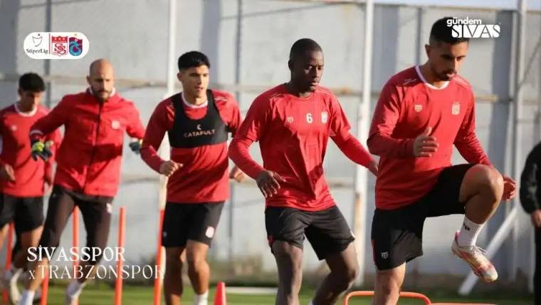 Kırmızı formalar giymiş futbolcular, antrenman sahasında koşu yapıyor.