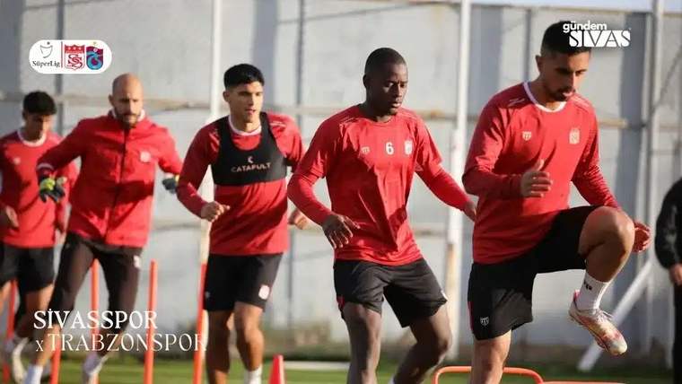 Kırmızı formalar giymiş futbolcular, antrenman sahasında koşu yapıyor.