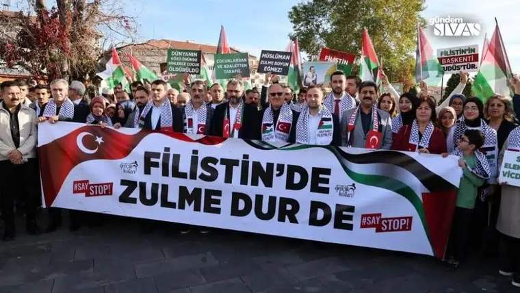 Filistin bayrakları ve pankartlarla yürüyüş yapan kalabalık bir grup, "Filistin'de zulme dur de" yazılı pankart taşıyor.