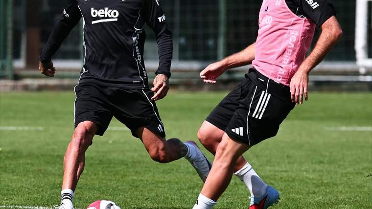 Beşiktaş forması giyen iki futbolcu, çim sahada top için mücadele ediyor.