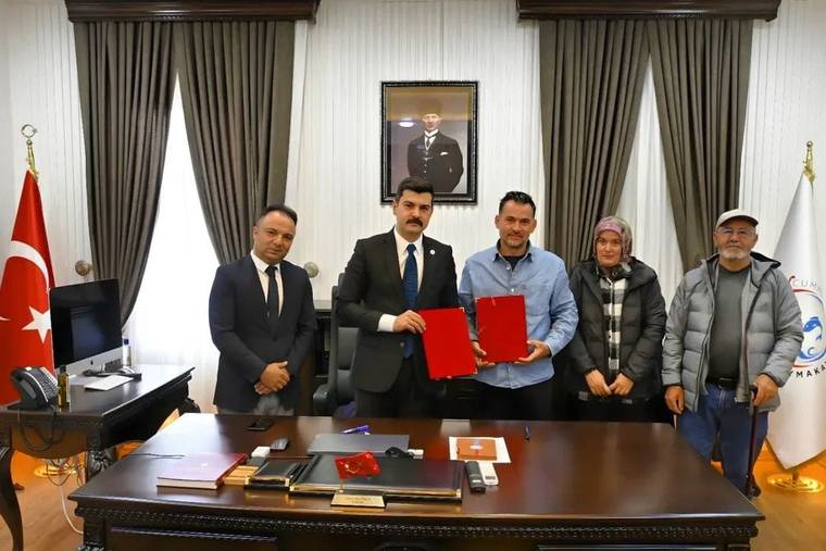 Bir masa etrafında duran beş kişi, elinde kırmızı dosya tutan bir kişiyle el sıkışıyor.
