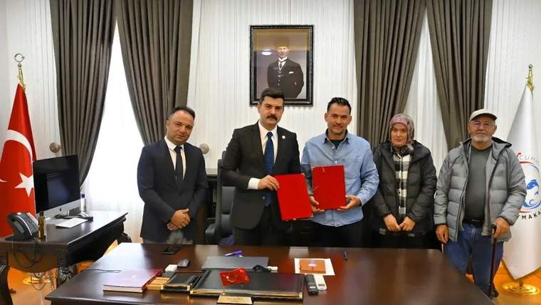 Bir masa etrafında duran beş kişi, elinde kırmızı dosya tutan bir kişiyle el sıkışıyor.