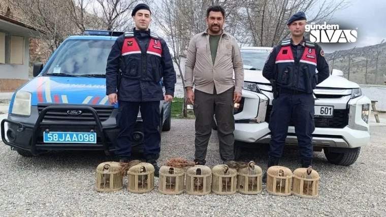 İki üniformalı görevli ve sivil bir kişi, araçların önünde kuş kafesleriyle birlikte duruyor.
