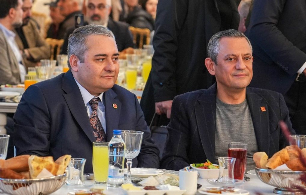 Kalabalık bir salonda masada oturan iki erkek, önlerindeki tabak ve içeceklerle birlikte görülüyor.