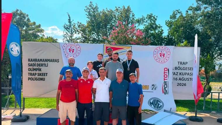 Açık havada bir grup kişi, üzerinde Kahramanmaraş ve trap skeet yazan pano önünde podyumda duruyor.